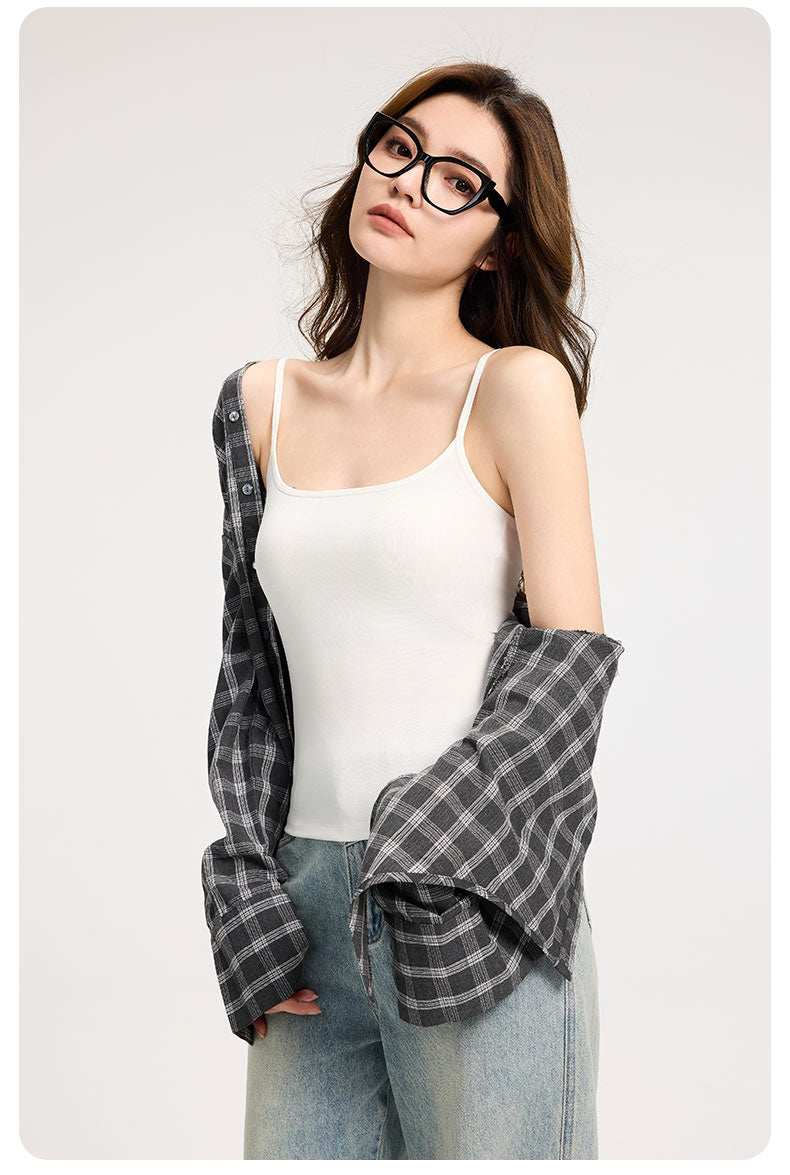 Woman wearing white slim-strap tank top with built-in bra and gray plaid shirt over shoulders