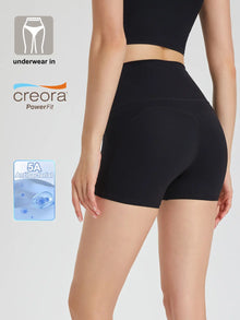 A pair of black Commando Chic Shorts with a mid-thigh length, featuring a seamless design and reflective back strips. The image also includes a close-up of the underwear's waistband detailing the 'Creora Powerfit' technology and a tag indicating '5A Antibacterial Protection'.