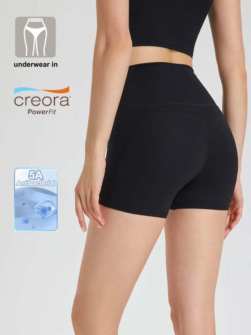 A pair of black Commando Chic Shorts with a mid-thigh length, featuring a seamless design and reflective back strips. The image also includes a close-up of the underwear's waistband detailing the 'Creora Powerfit' technology and a tag indicating '5A Antibacterial Protection'.